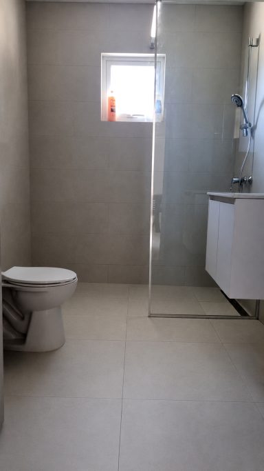 Eenvoudige badkamer met toilet, wastafel en douchecabine. Natuurlijke verlichting van het raam.